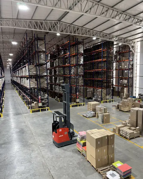 Pasillo de la nave de LMC con racks de 12 metros cargados de pallets hasta arriba y un autoelevador en el centro